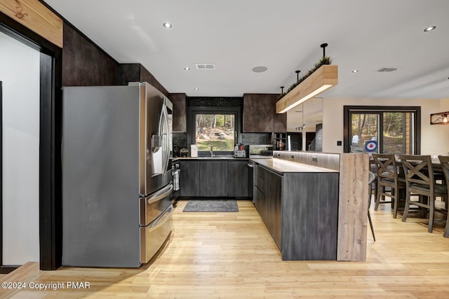 kitchen featuring stainless steel refrigerator with ice dispenser, light wood finished floors, visible vents, modern cabinets, and a peninsula