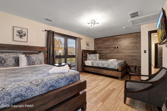 bedroom featuring an accent wall, visible vents, wood walls, and wood finished floors