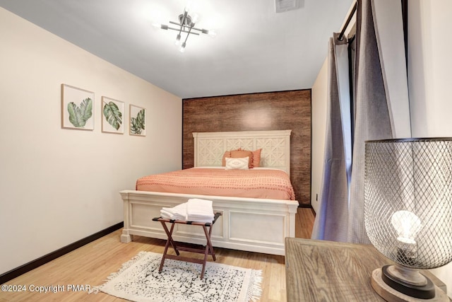 bedroom with an accent wall, visible vents, baseboards, and wood finished floors