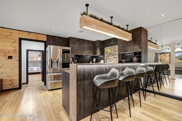 kitchen featuring stainless steel fridge with ice dispenser, modern cabinets, a breakfast bar area, dark brown cabinets, and light wood-style floors