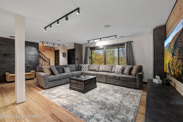 living area with visible vents, an accent wall, stairway, wood finished floors, and track lighting