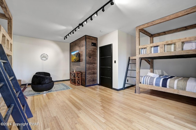 bedroom with wood finished floors, rail lighting, and baseboards