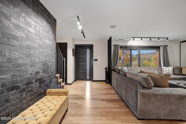 living area with baseboards, light wood-style flooring, an accent wall, stairway, and rail lighting