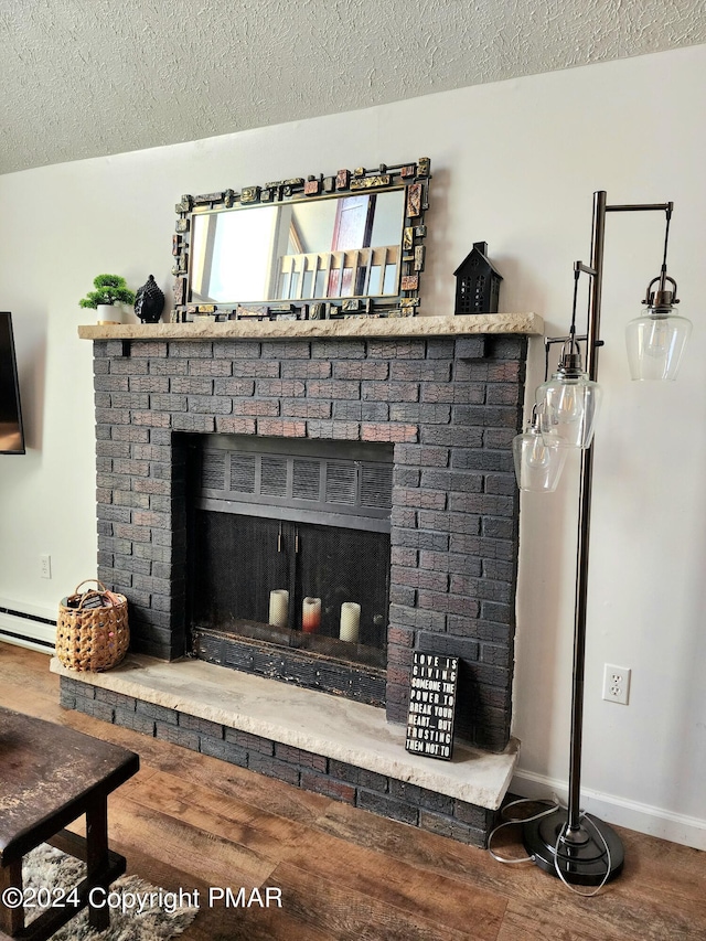 room details featuring hardwood / wood-style flooring, a baseboard radiator, a brick fireplace, and a textured ceiling