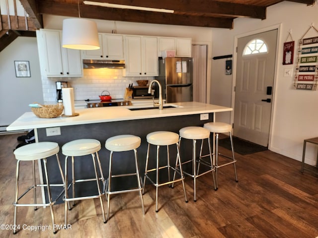 kitchen with beamed ceiling, a sink, under cabinet range hood, stainless steel appliances, and dark wood-style flooring