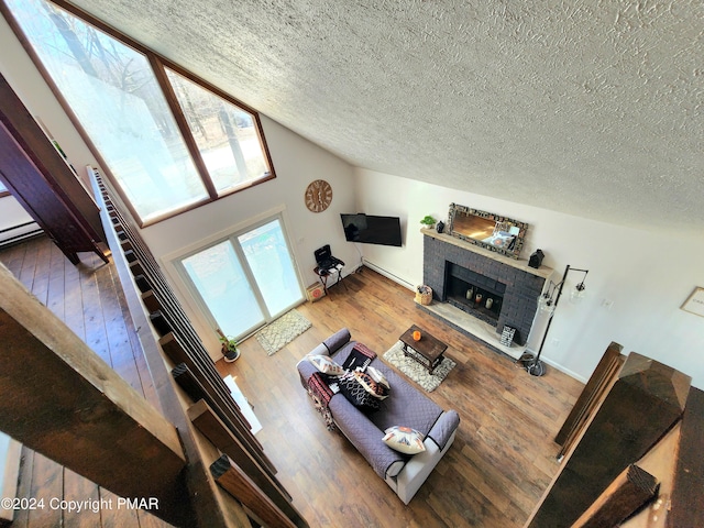 living room with hardwood / wood-style flooring, a tile fireplace, lofted ceiling, and a textured ceiling