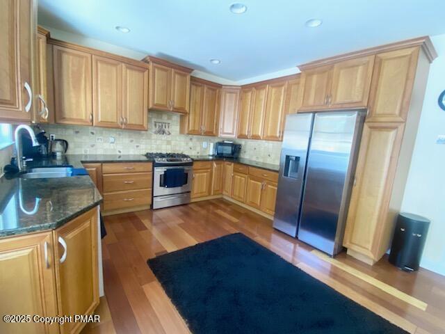 kitchen with sink, dark stone countertops, light hardwood / wood-style flooring, backsplash, and stainless steel appliances