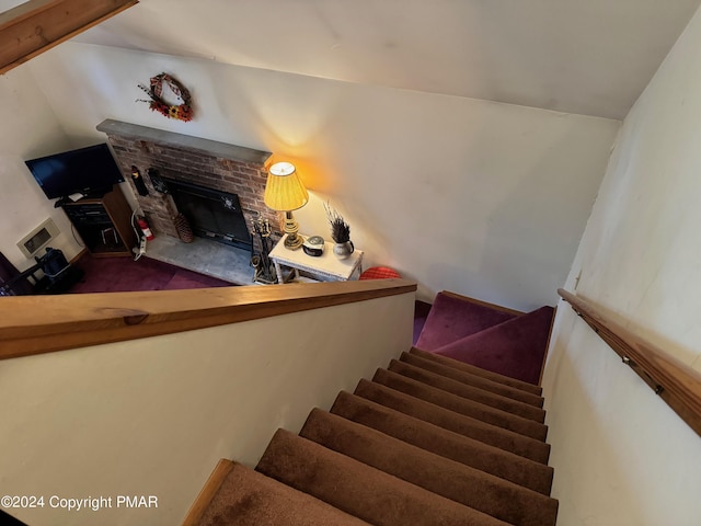 stairs with lofted ceiling and a fireplace