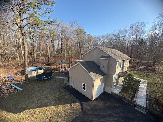 5109 Hickory Ln, East Stroudsburg, PA 18302 - view of side of home featuring a lawn, a shingled roof, aphalt driveway, and a trampoline