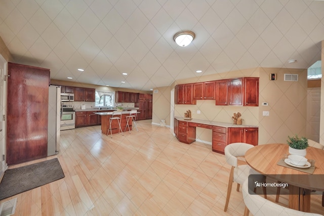 205 Osprey Way E, Stroudsburg, PA 18302 - kitchen featuring reddish brown cabinets, appliances with stainless steel finishes, a breakfast bar area, light countertops, and recessed lighting
