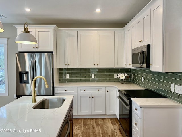 kitchen with appliances with stainless steel finishes, white cabinetry, a sink, and light stone countertops