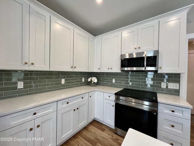 kitchen with backsplash, white cabinetry, stainless steel appliances, and wood finished floors