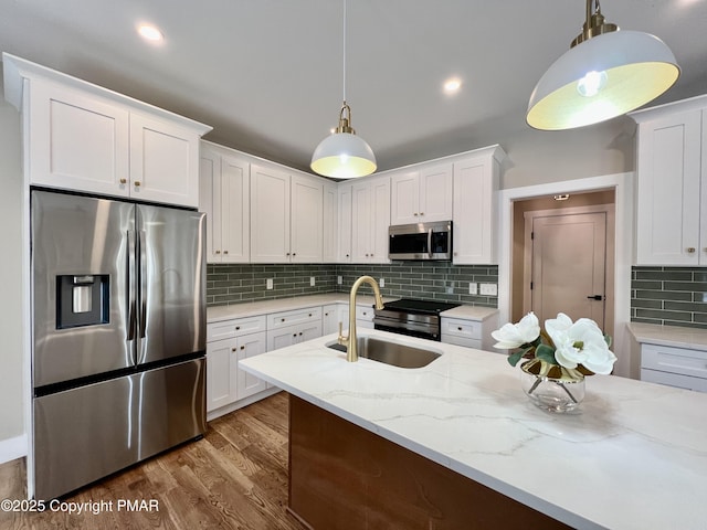 kitchen with pendant lighting, appliances with stainless steel finishes, white cabinetry, a sink, and wood finished floors