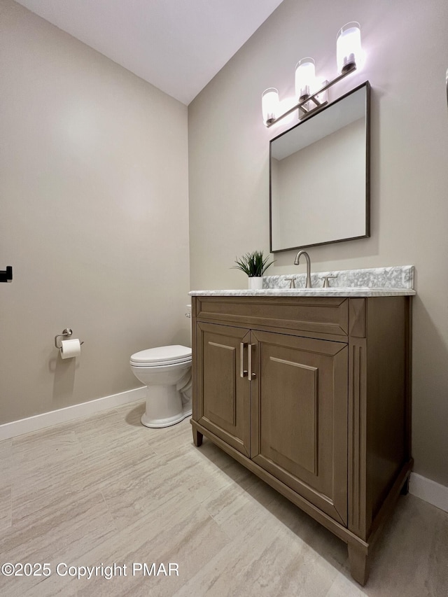 half bathroom with toilet, baseboards, and vanity