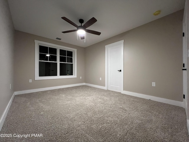 empty room with carpet floors, a ceiling fan, visible vents, and baseboards