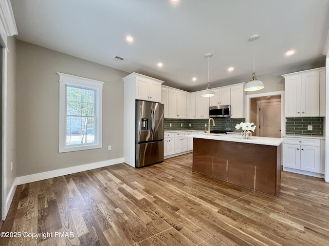 kitchen with wood finished floors, white cabinets, light countertops, appliances with stainless steel finishes, and tasteful backsplash