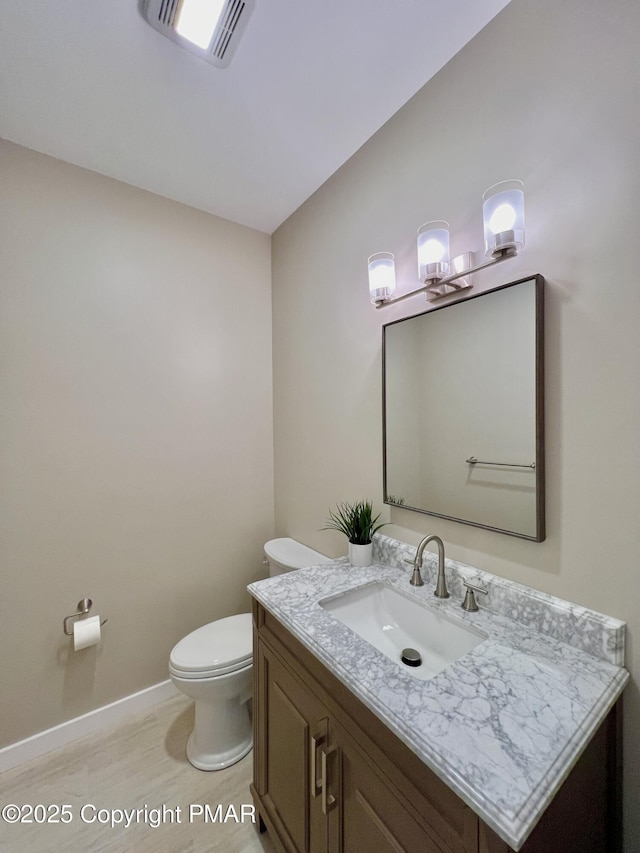 half bath featuring baseboards, visible vents, vanity, and toilet