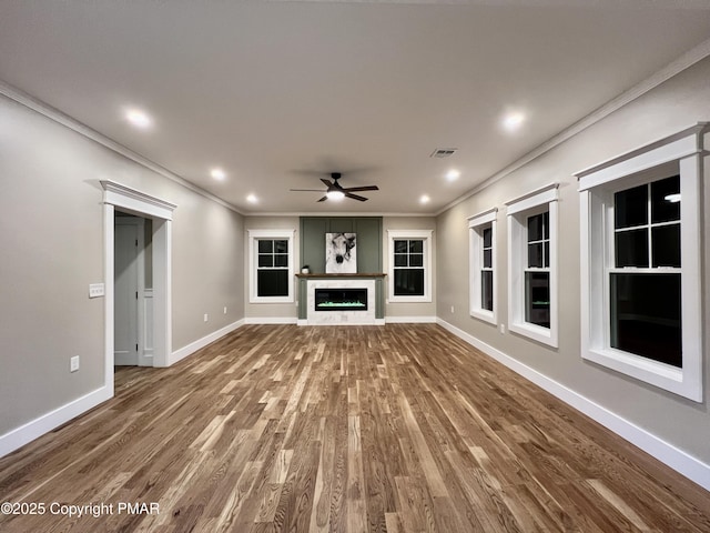 unfurnished living room with baseboards, wood finished floors, crown molding, and a glass covered fireplace