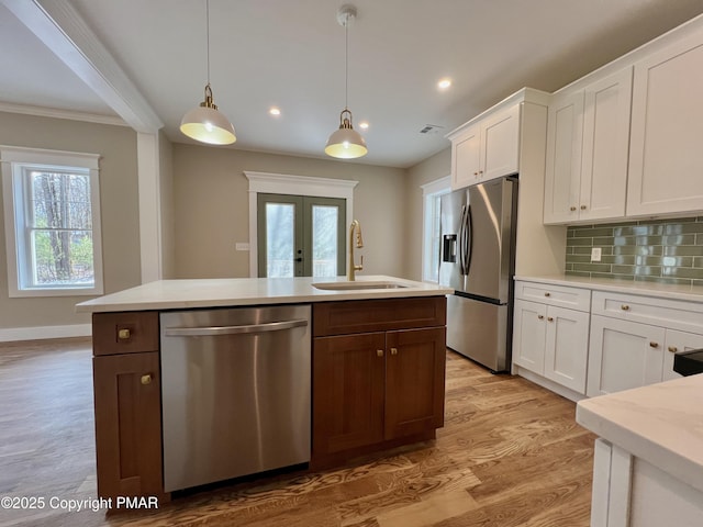 kitchen with stainless steel appliances, a sink, white cabinets, french doors, and decorative backsplash