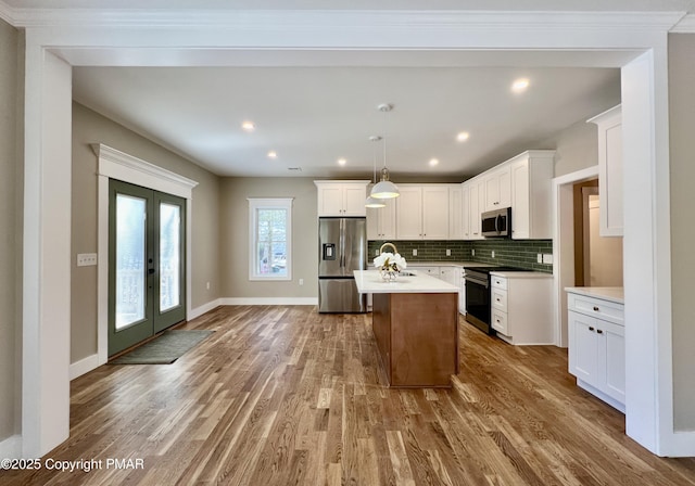 kitchen with wood finished floors, stainless steel appliances, light countertops, french doors, and backsplash