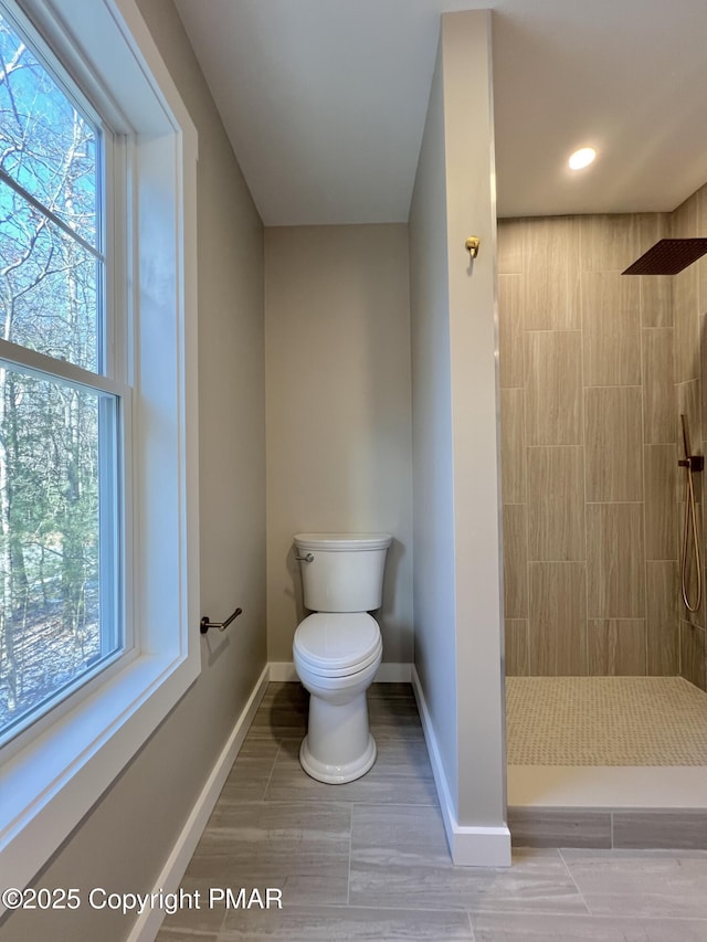 full bath with tiled shower, plenty of natural light, toilet, and baseboards