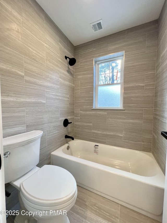 full bathroom with toilet, shower / bath combination, visible vents, and tile walls