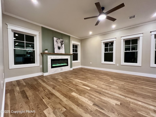 unfurnished living room with a premium fireplace, visible vents, wood finished floors, and ornamental molding