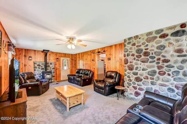 living room featuring carpet floors, wood walls, a wood stove, and a ceiling fan