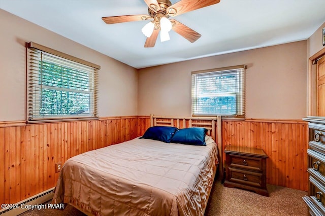 carpeted bedroom featuring wood walls, multiple windows, a baseboard heating unit, and wainscoting