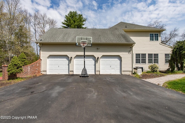 view of front facade featuring driveway, a shingled roof, an attached garage, and cooling unit