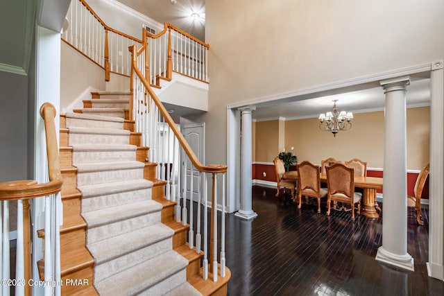 stairs with wood-type flooring, a high ceiling, ornamental molding, a chandelier, and ornate columns