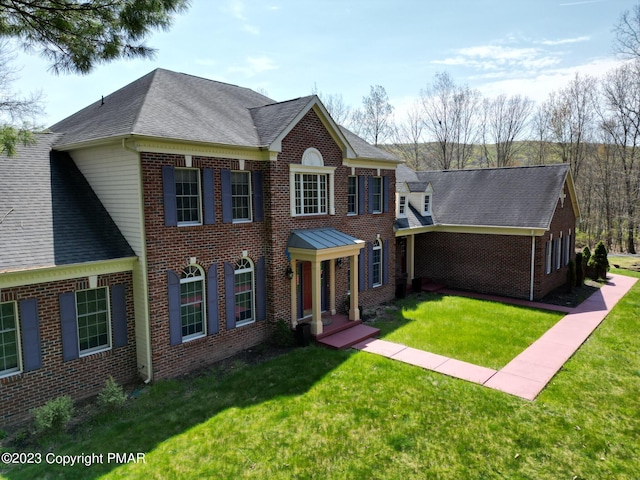 georgian-style home with brick siding, a front lawn, and roof with shingles