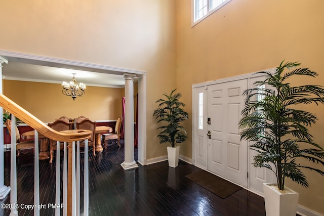 entryway featuring decorative columns, baseboards, ornamental molding, dark wood-style flooring, and a notable chandelier