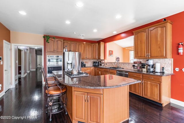 kitchen featuring stainless steel appliances, a sink, a center island, decorative backsplash, and a kitchen bar