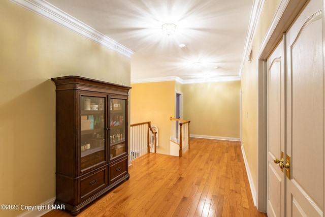 corridor featuring baseboards, ornamental molding, an upstairs landing, and light wood-style floors