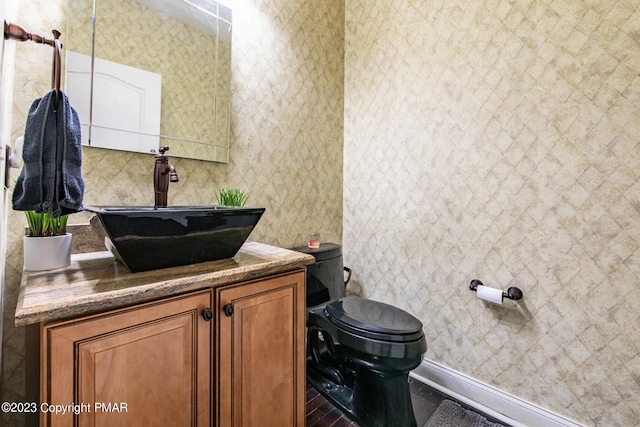 half bath with baseboards, vanity, and toilet