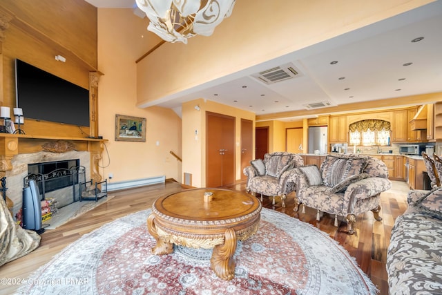 living area featuring a baseboard radiator, visible vents, light wood-style flooring, an inviting chandelier, and a large fireplace