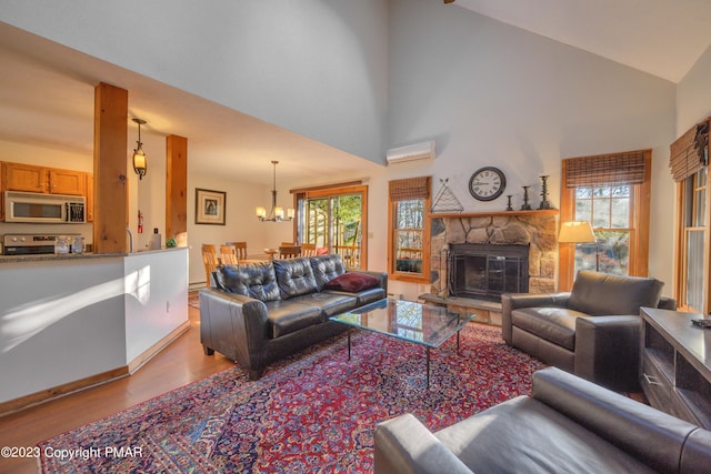 living room with a chandelier, high vaulted ceiling, a stone fireplace, an AC wall unit, and wood finished floors