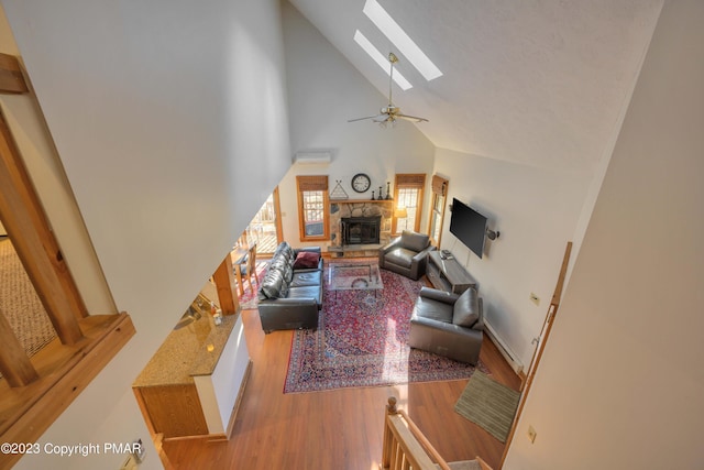 living area featuring high vaulted ceiling, a ceiling fan, a stone fireplace, a skylight, and wood finished floors