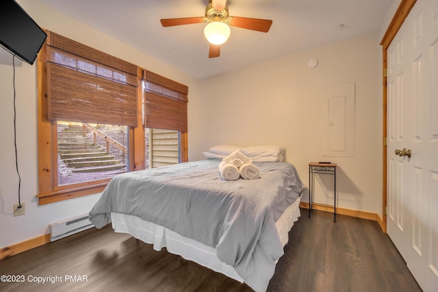 bedroom featuring a baseboard heating unit, a closet, ceiling fan, baseboards, and wood finished floors