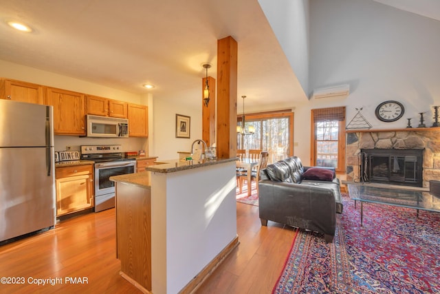 kitchen with light wood finished floors, stainless steel appliances, a wall mounted air conditioner, stone counters, and open floor plan