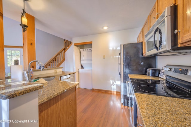 kitchen featuring a sink, stainless steel appliances, stacked washer and clothes dryer, stone countertops, and wood finished floors