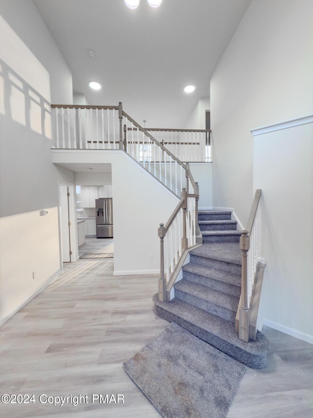 staircase featuring recessed lighting, baseboards, a high ceiling, and wood finished floors