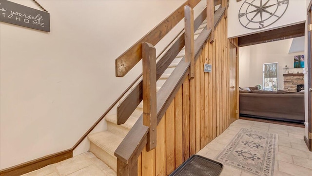 stairway featuring beamed ceiling, a fireplace, and wood walls