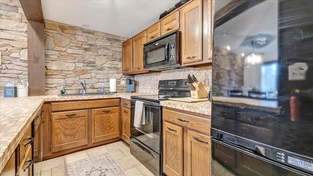 kitchen with brown cabinetry, a sink, black appliances, tile counters, and backsplash