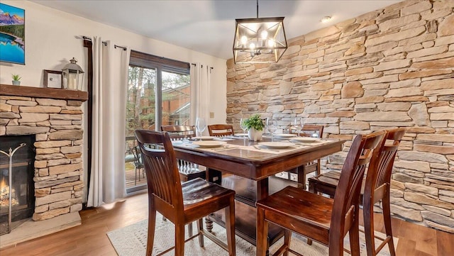 dining room featuring a notable chandelier, a stone fireplace, and wood finished floors