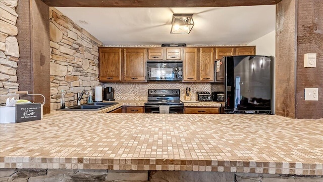 kitchen featuring tasteful backsplash, light countertops, a peninsula, black appliances, and a sink