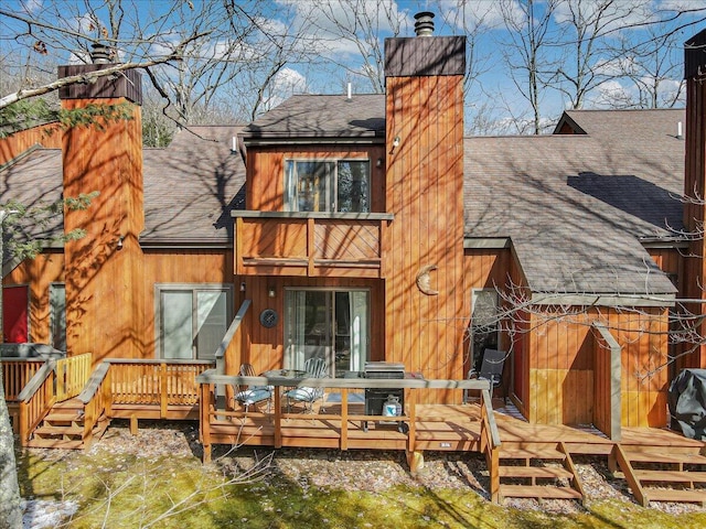 back of house featuring roof with shingles, a deck, and a chimney