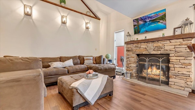 living area featuring a stone fireplace, lofted ceiling, and wood finished floors