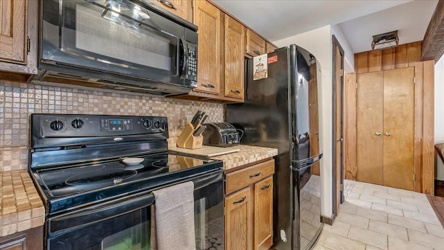 kitchen with light countertops, light tile patterned floors, decorative backsplash, brown cabinetry, and black appliances